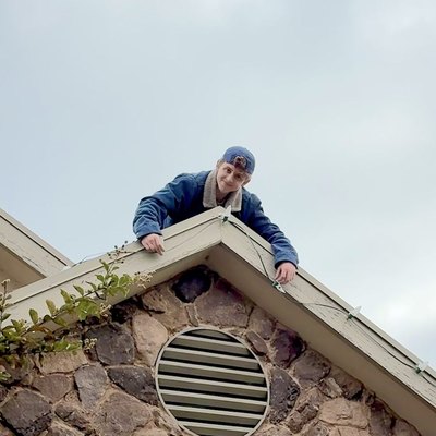 Zach leaning over a roof peak while clipping C9 lights to the edge