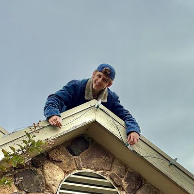 Zach smiling as he leans over a roof peak while clipping C9 lights to the edge